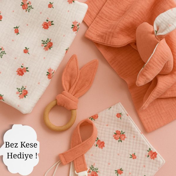 Organik Müslin Bebek Uyku Seti, pembe çiçek desenli pembe müslin örtü, uyumlu önlük, pembe müslin kundak ve mavi tavşan kulaklı ahşap diş kaşıyıcıdan oluşuyor.