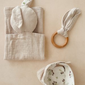 Organik Müslin Bebek Uyku Seti, bej çiçek desenli bej müslin örtü, uyumlu önlük, bej müslin kundak ve bej tavşan kulaklı ahşap diş kaşıyıcıdan oluşuyor.